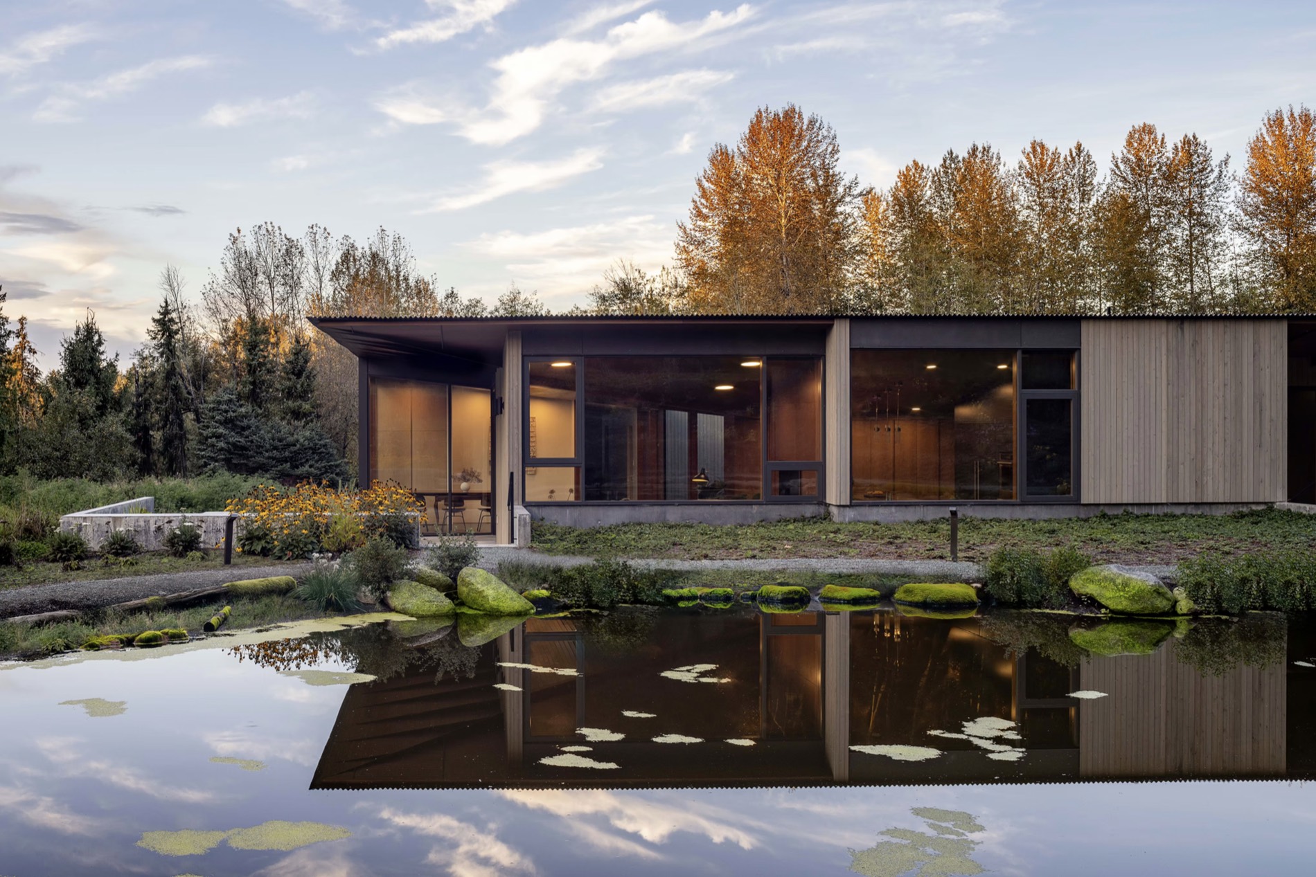 A low timber house in the forest, mirrored in a still pond